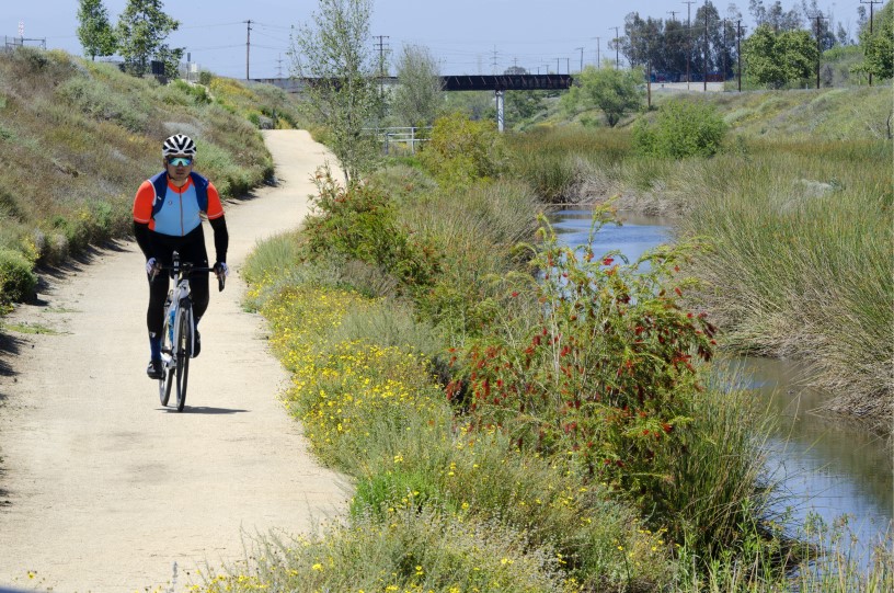 A thumbnail of a person riding a bike down a dirt path next to a creek with vegetation and flowers that provides more information about the topic Water quality and supplies